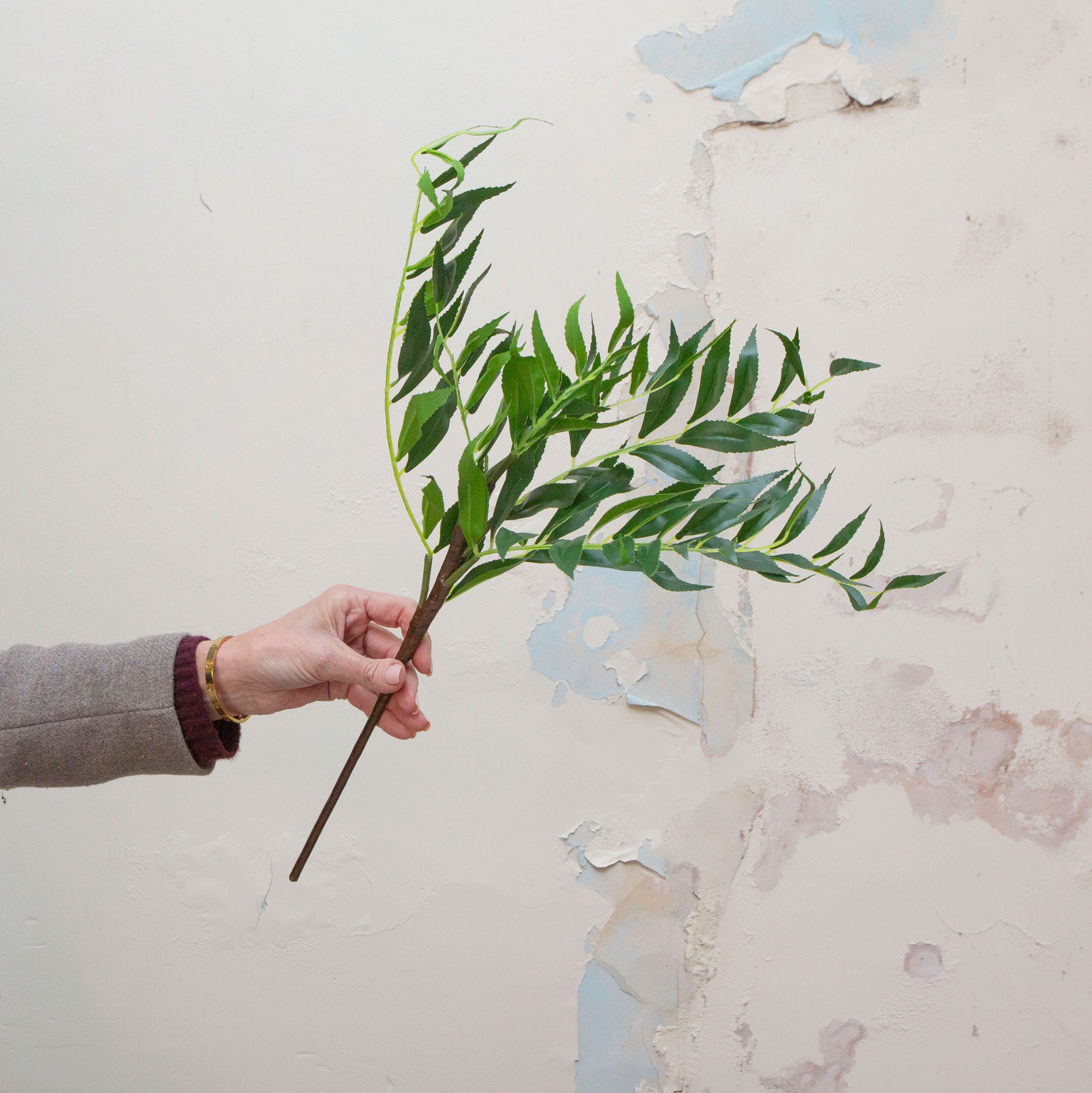 Hand holding artificial greenery leaves spray
