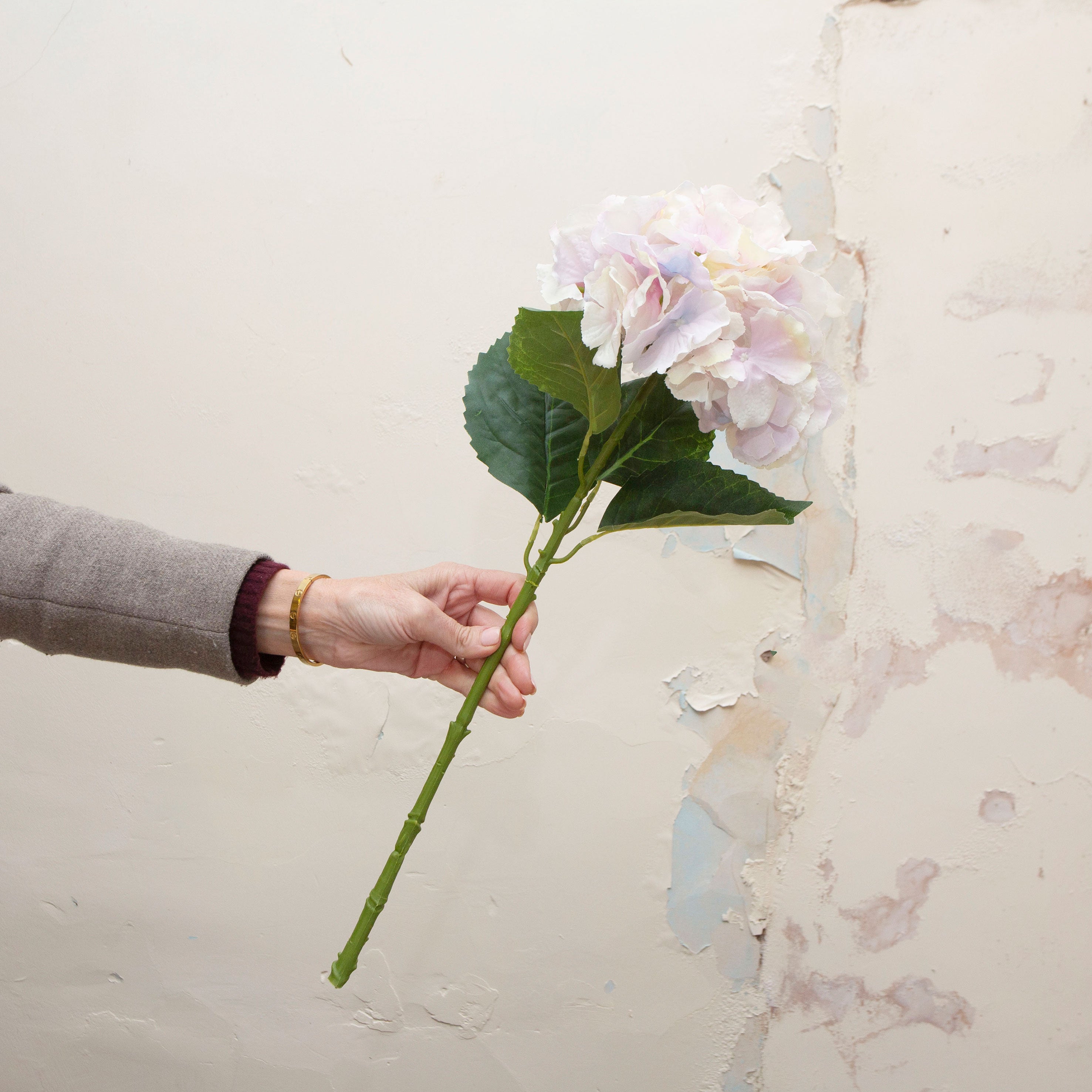 Hand holding a large headed artificial hydrangea stem with pale lilac and cream mixed petals