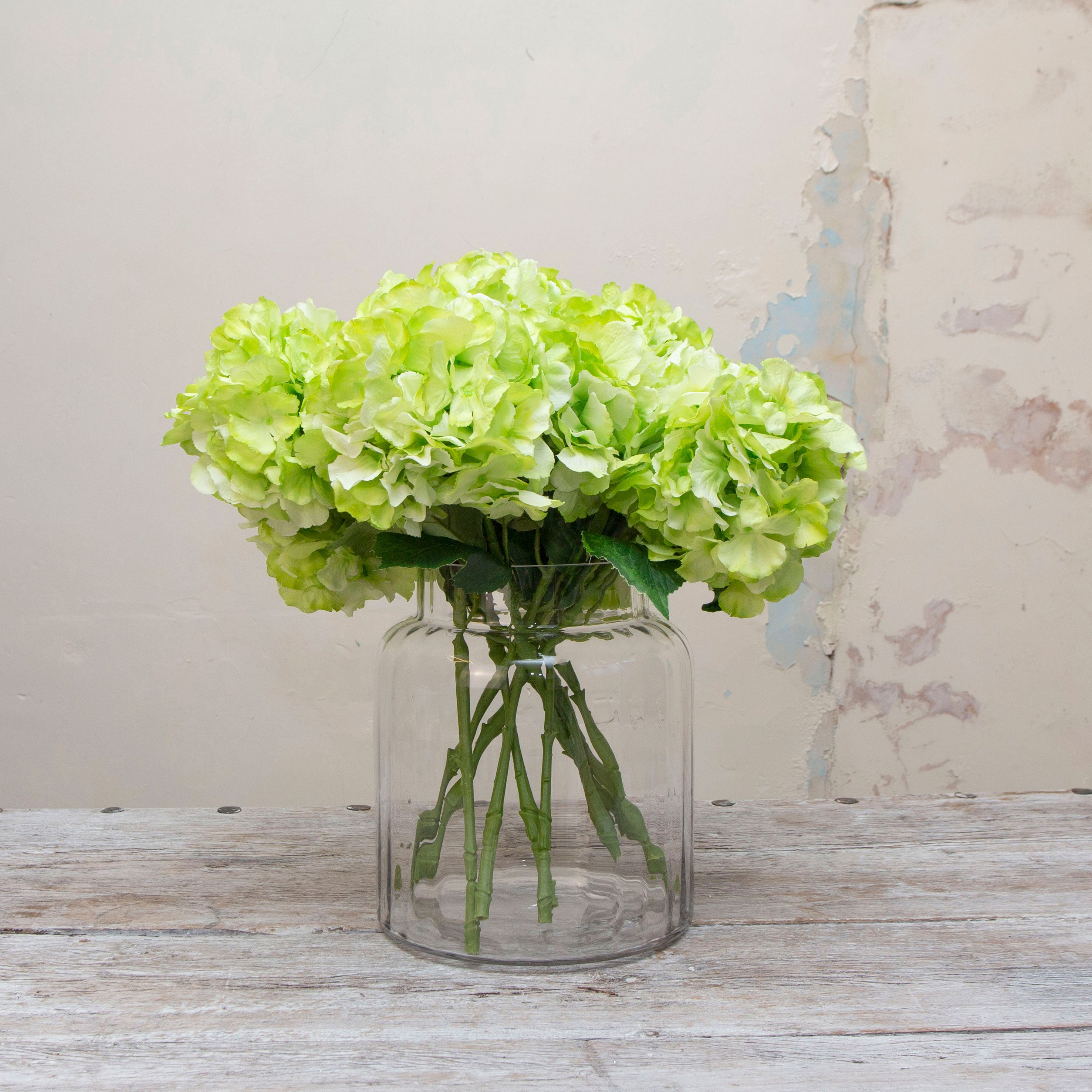 Large headed artificial bright lime green hydrangea stems with leaves displayed in vase
