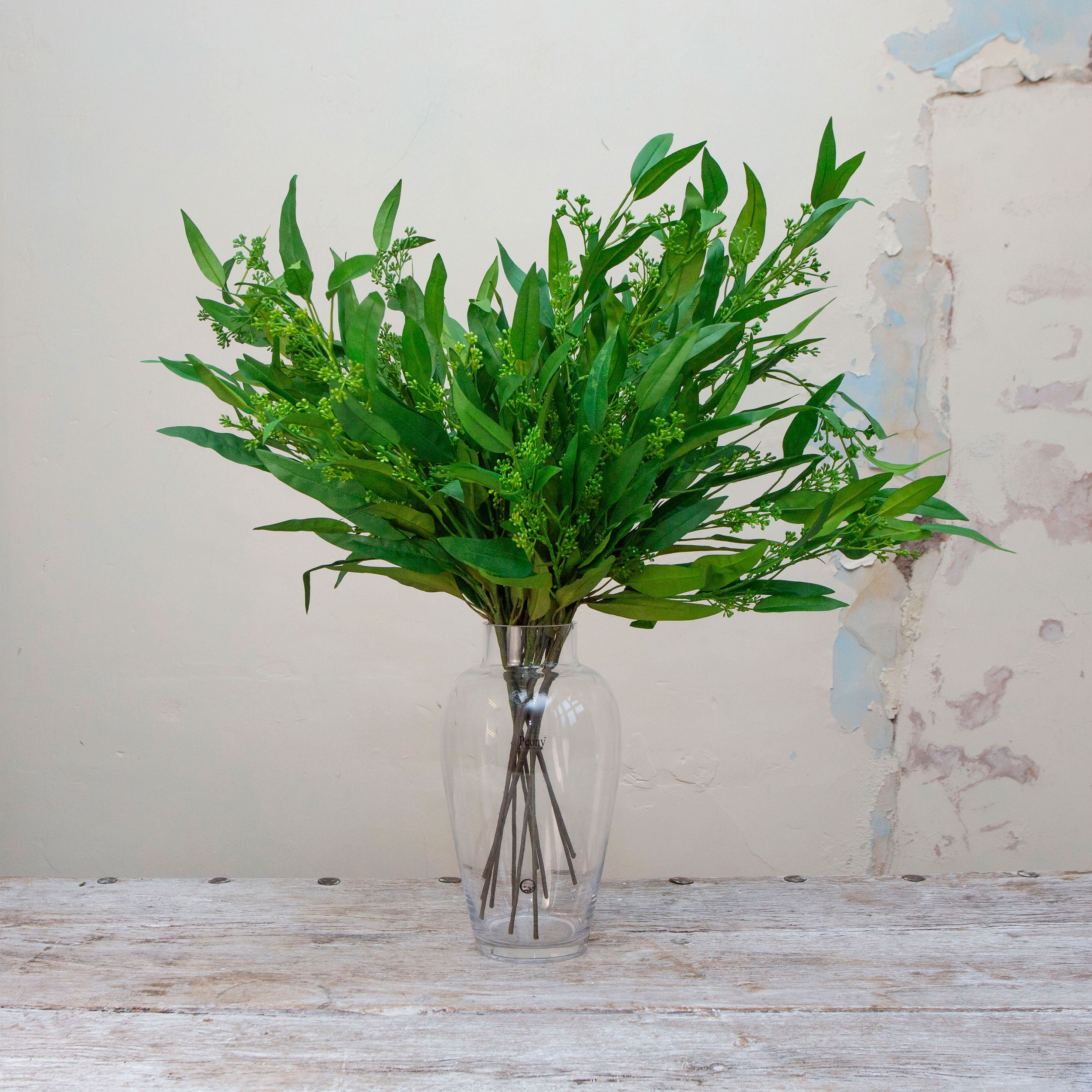 Artificial green long leaf eucalyptus stems with seeds displayed in vase