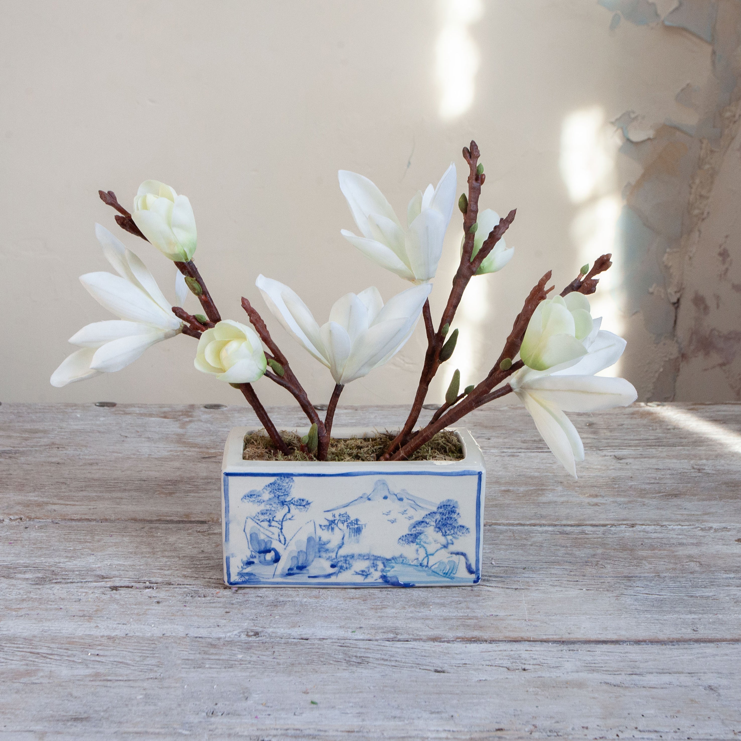 Artificial magnolia arrangement with white blooms displayed in a blue and white ceramic planter.