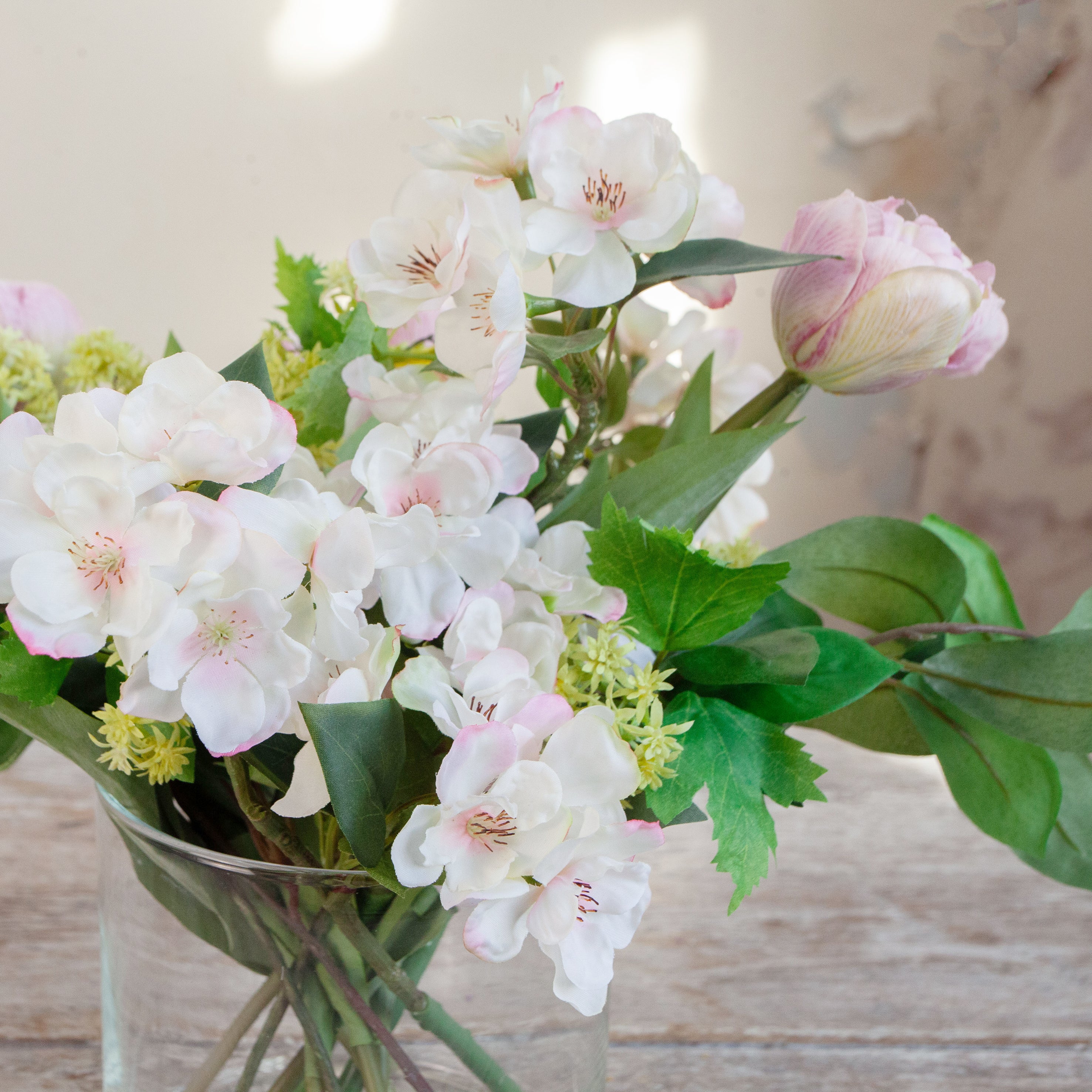Artificial tulip and blossom arrangement with colourful spring blooms displayed in a clear cylinder glass vase.