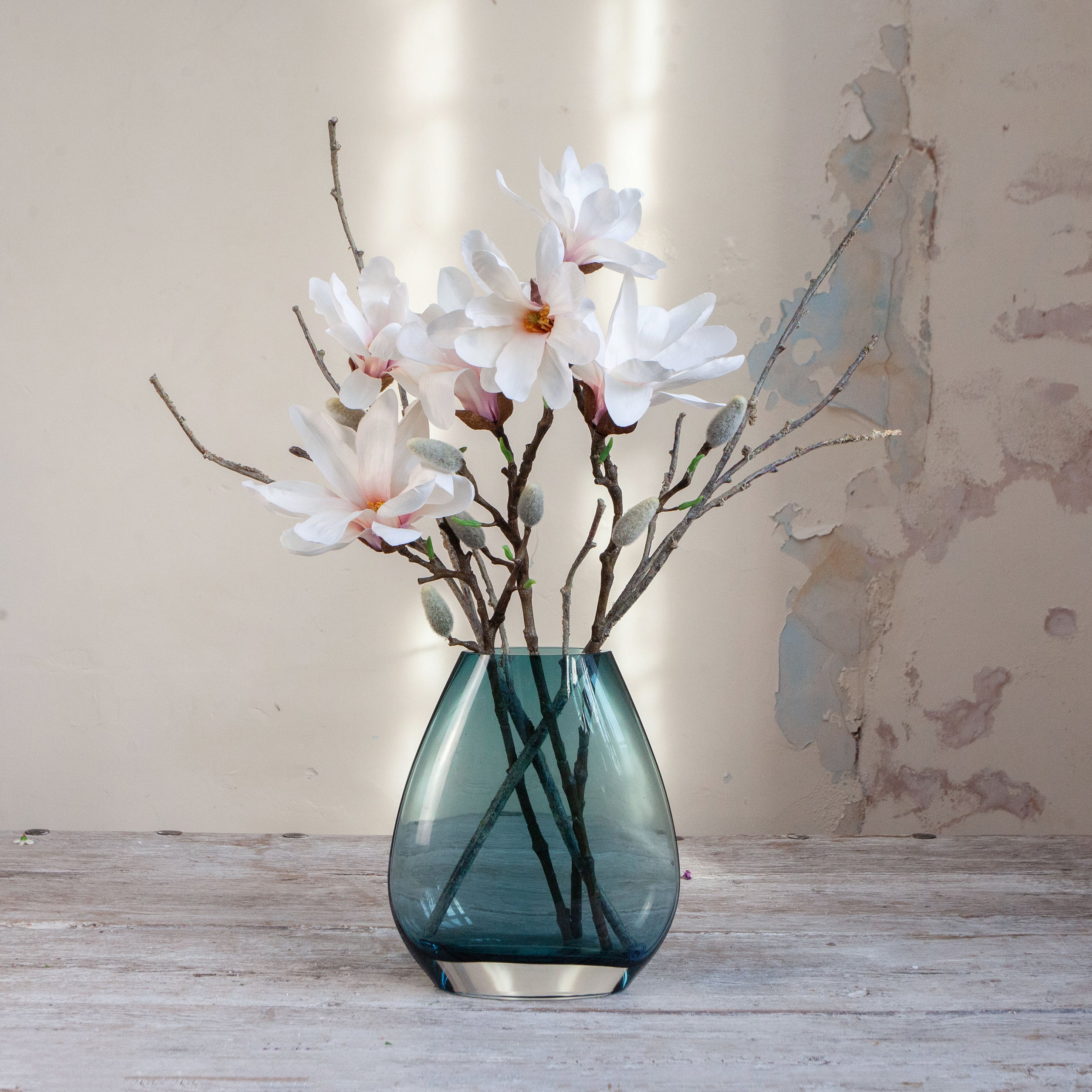 Artificial magnolia and branch arrangement with soft white blooms displayed in an ocean blue glass vase.