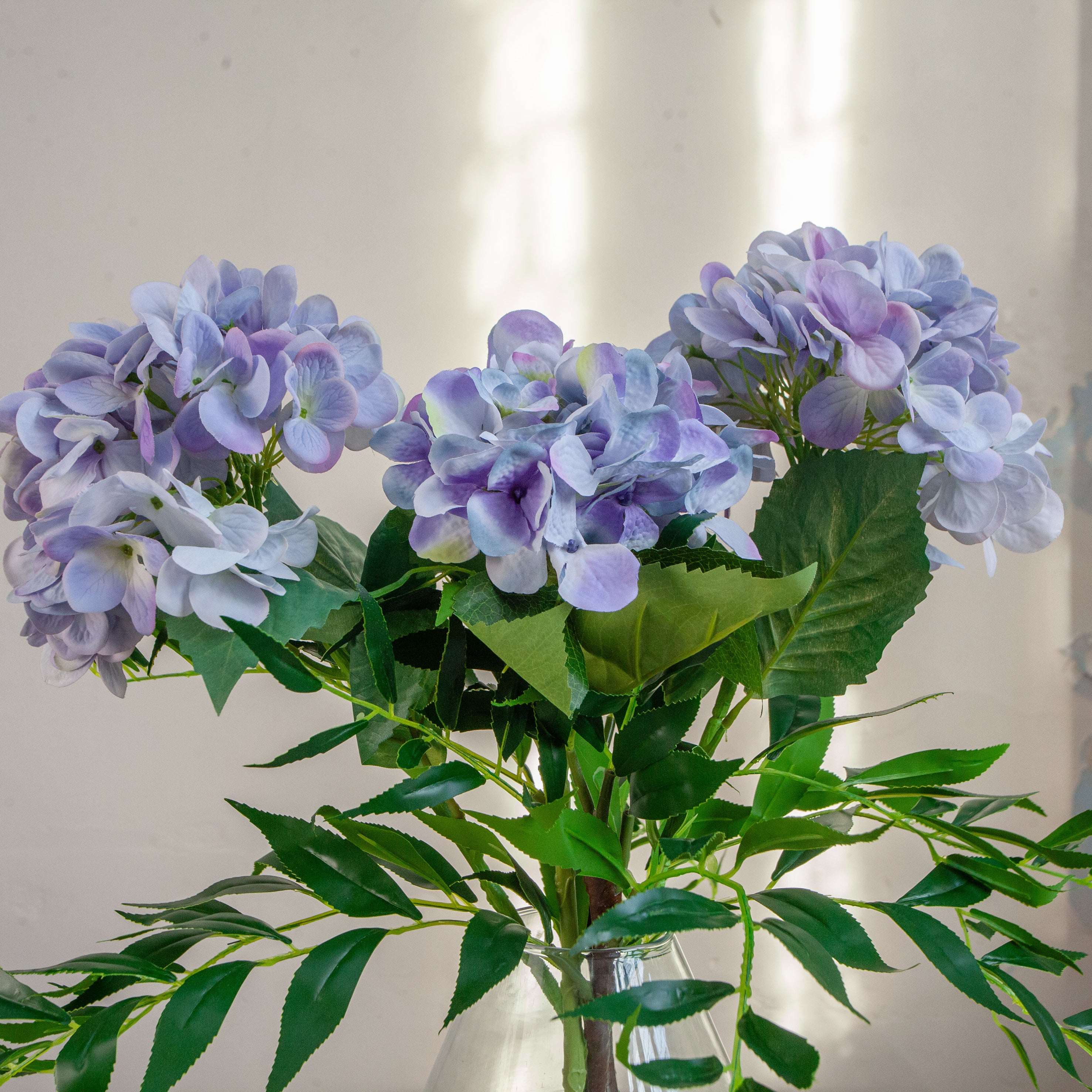 Artificial hydrangea and greenery arrangement in a teardrop-shaped vase,