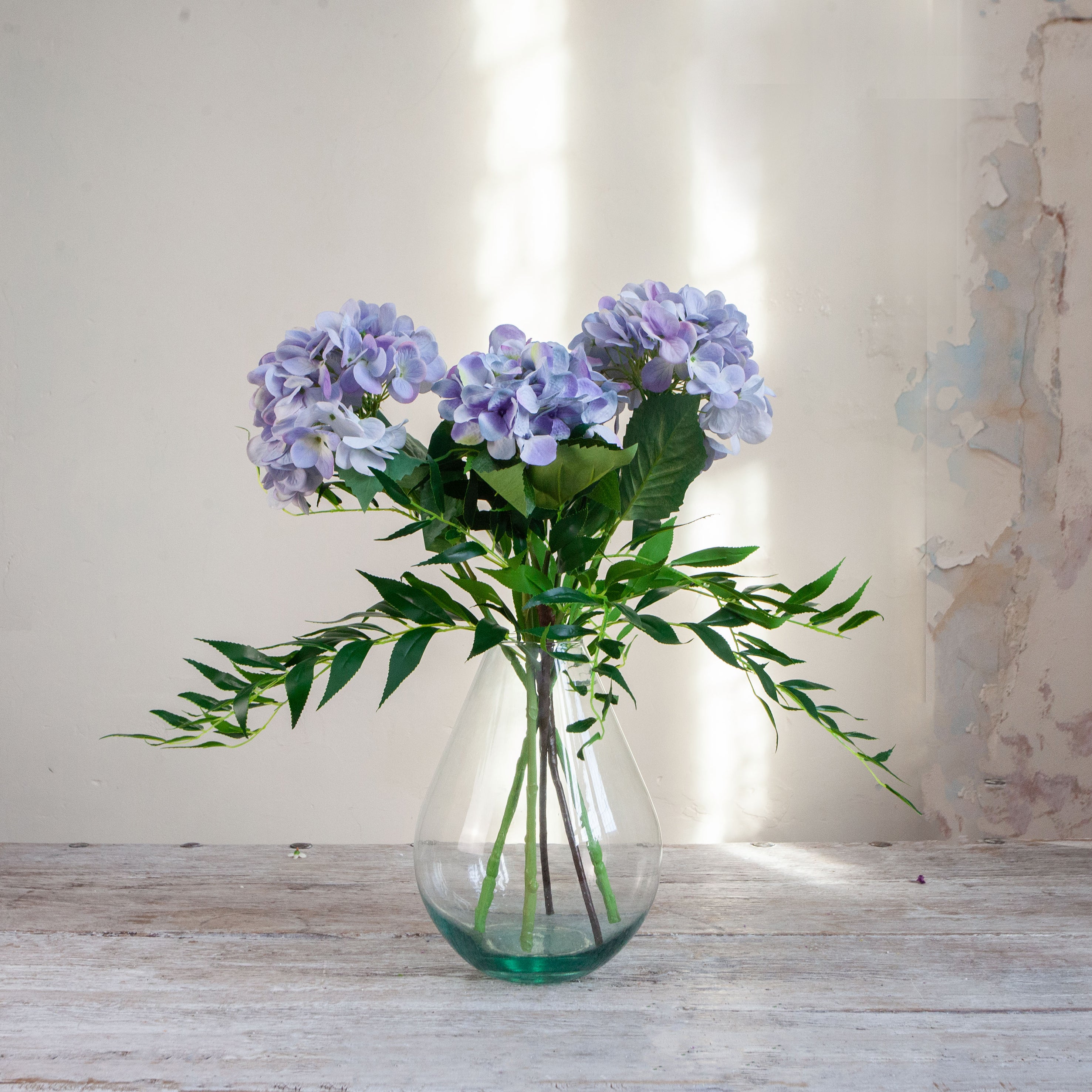 Artificial hydrangea and greenery arrangement in a teardrop-shaped vase,