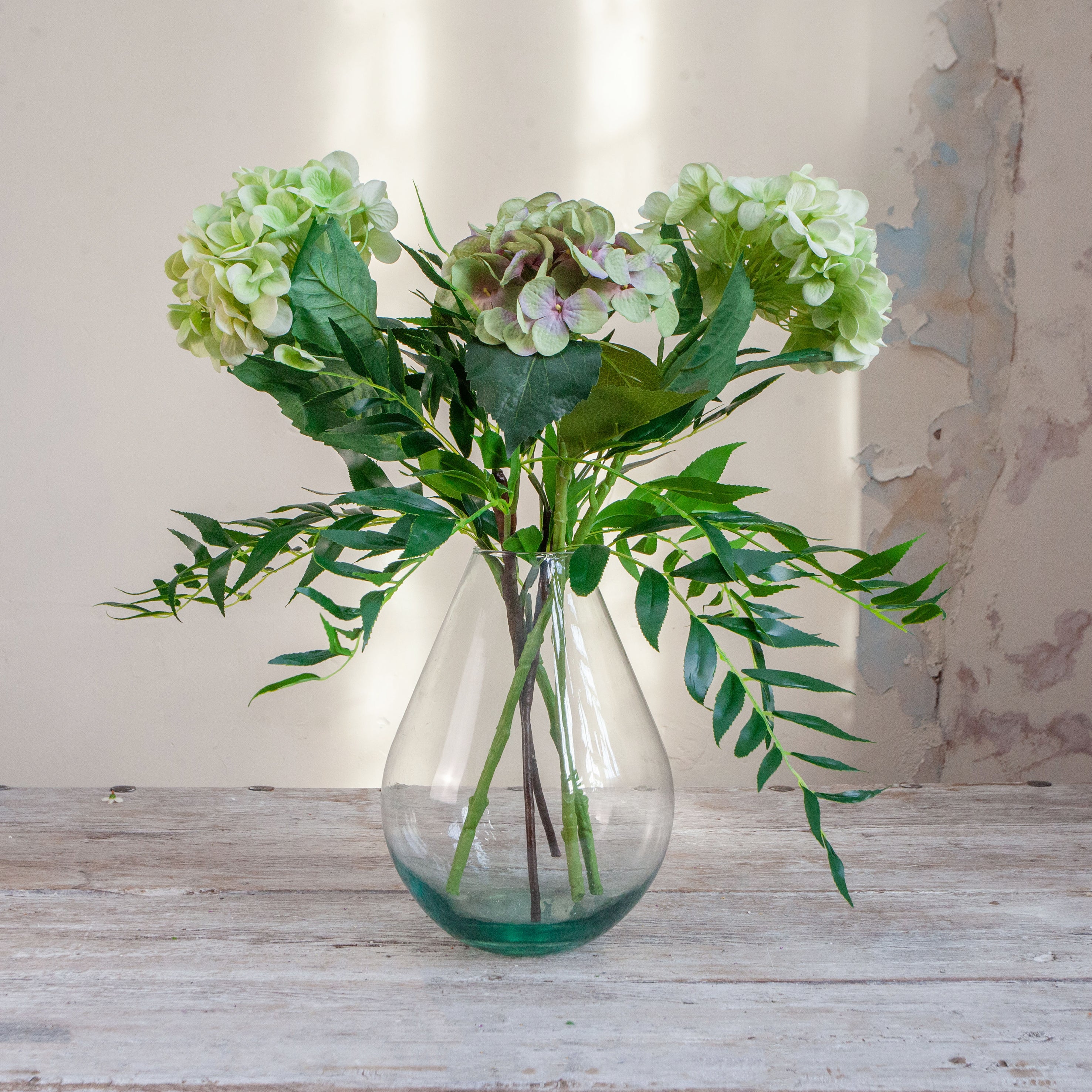 Artificial hydrangea and greenery arrangement in a teardrop-shaped vase,