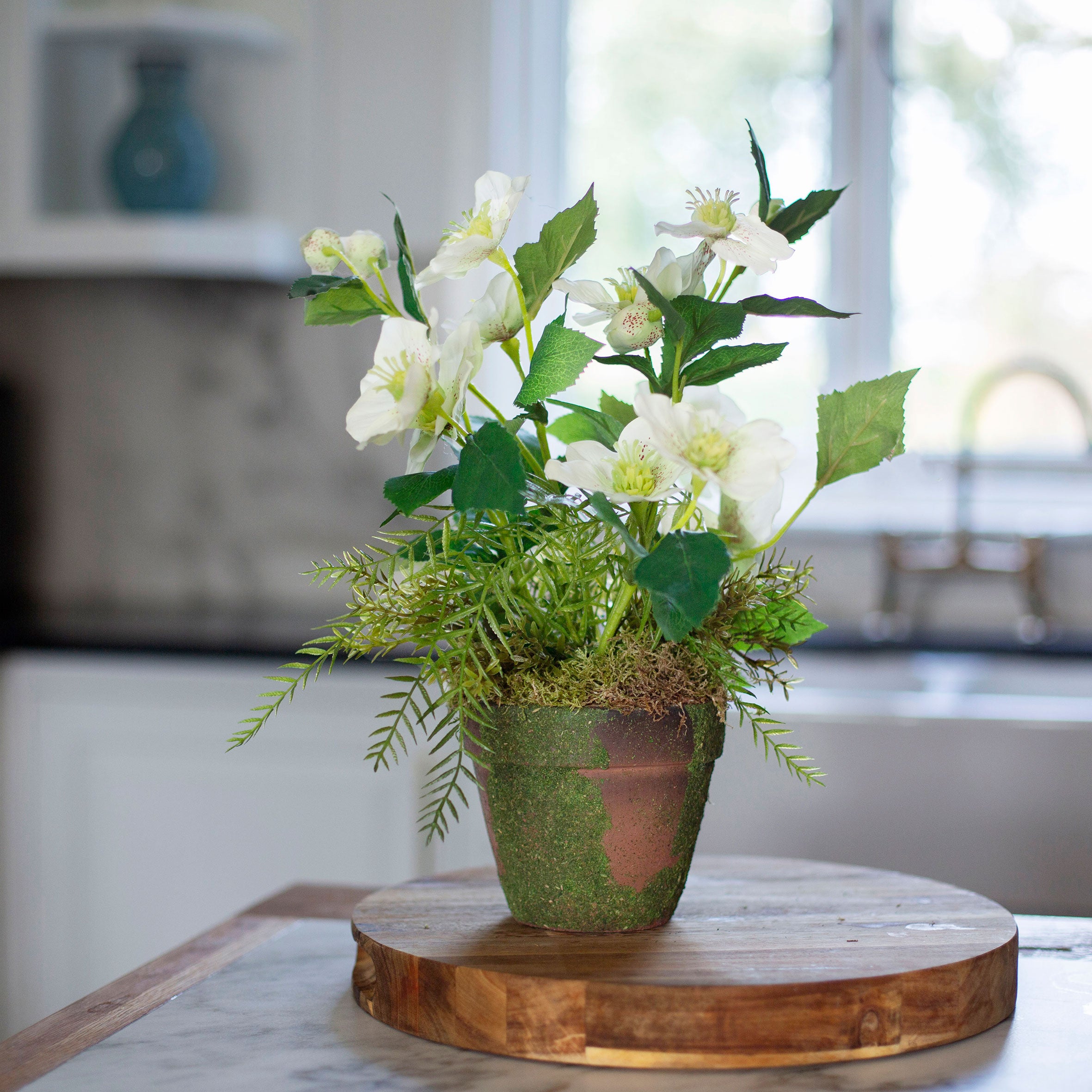 Artficial hellebore flowers arranged in a moss pot with foliage and willow