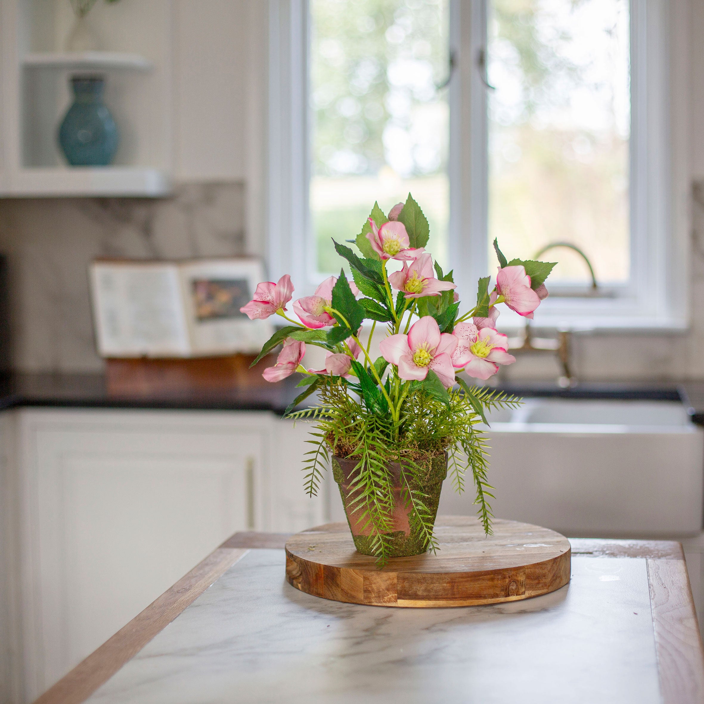 Artficial hellebore flowers arranged in a moss pot with foliage and willow
