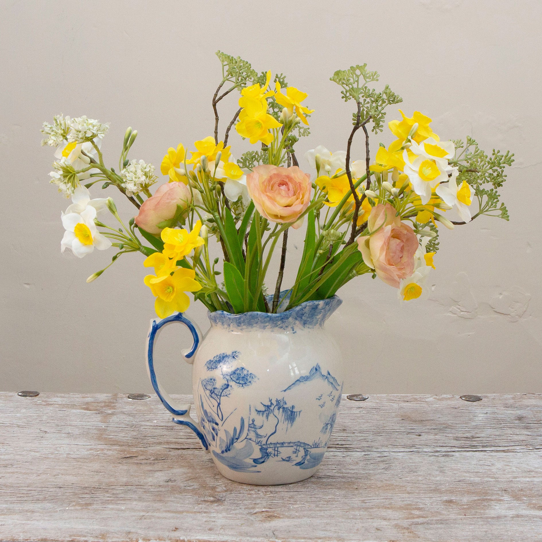 Artificial daffodil and ranunculus flower arrangement in a blue and white hand painted oriental jug