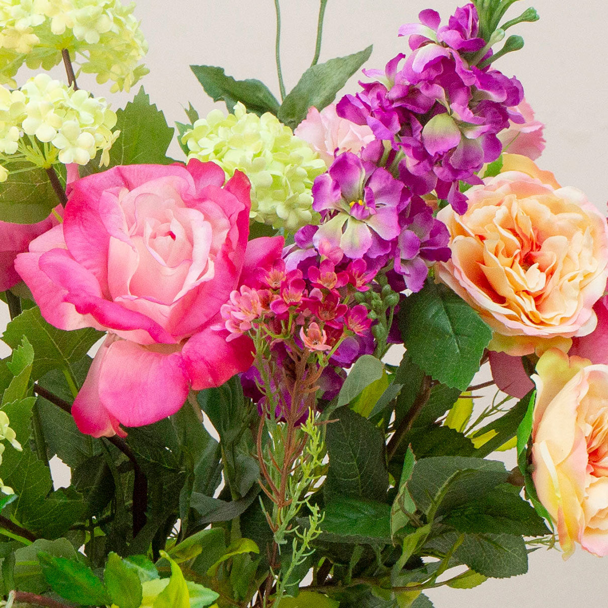 Artificial rose and stock summer flower arrangement in a clear grand waisted glass vase