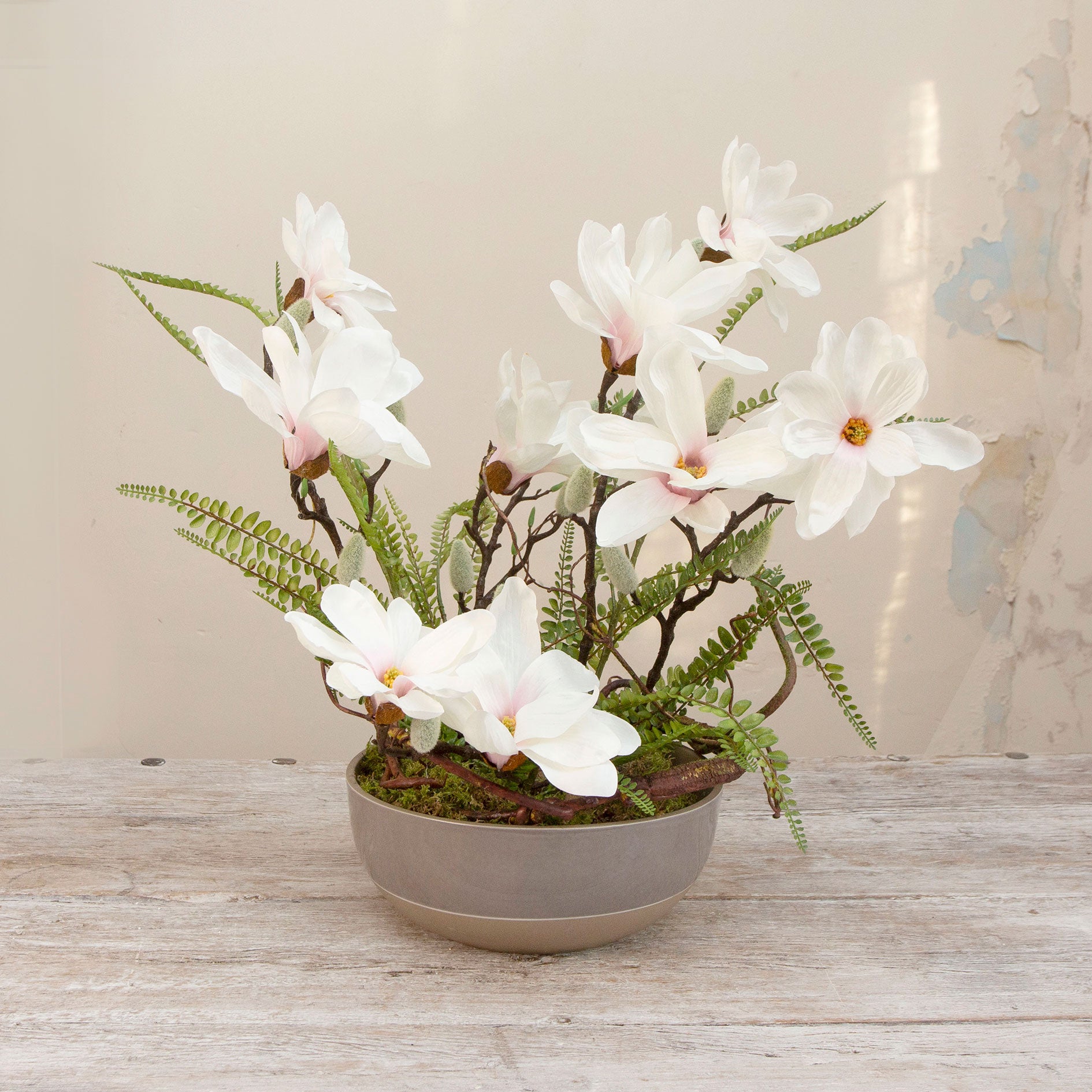 Artificial magnolia flowers and ferns arranged in a low grey banded bowl