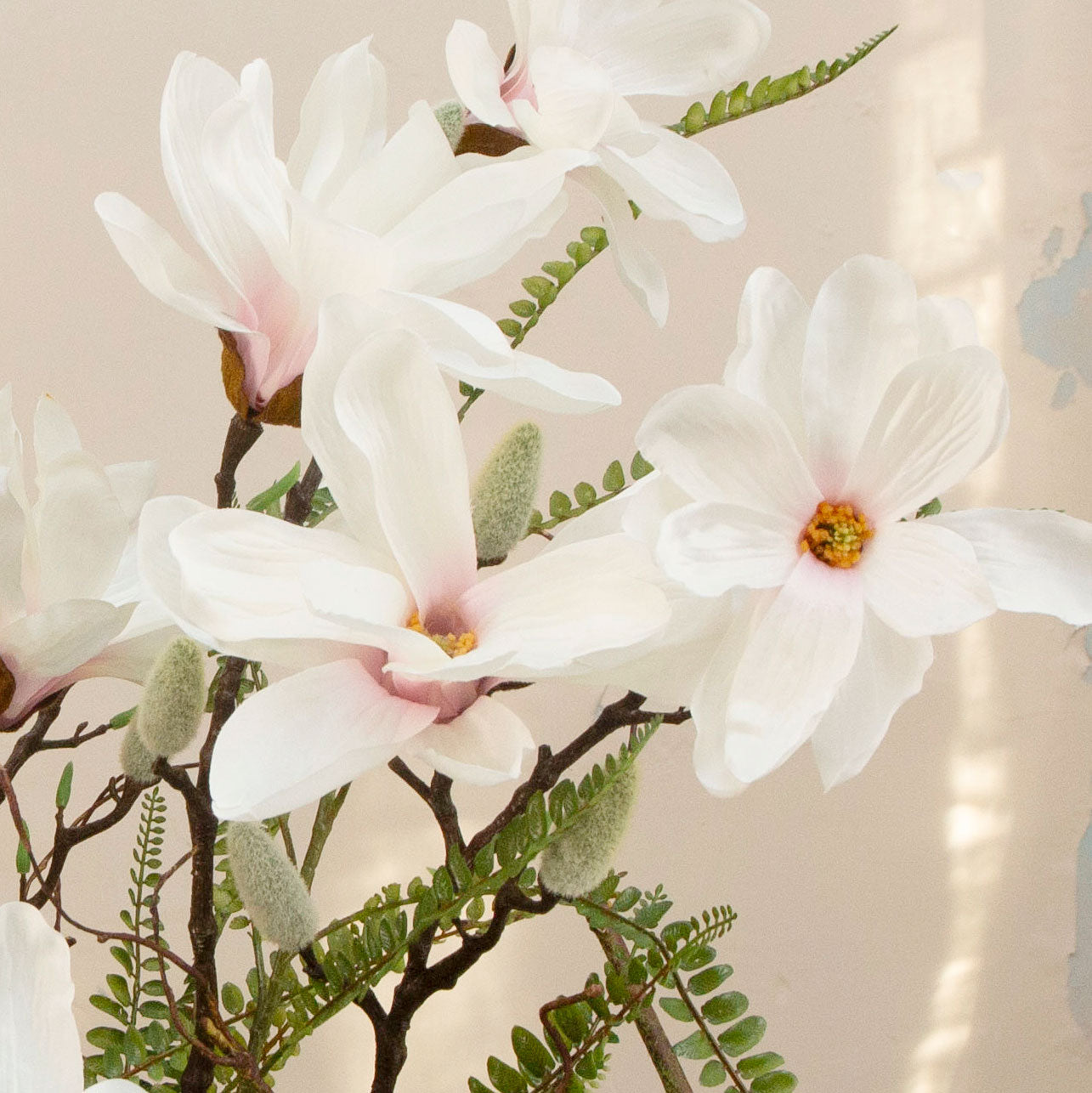 Artificial magnolia flowers and ferns arranged in a low grey banded bowl