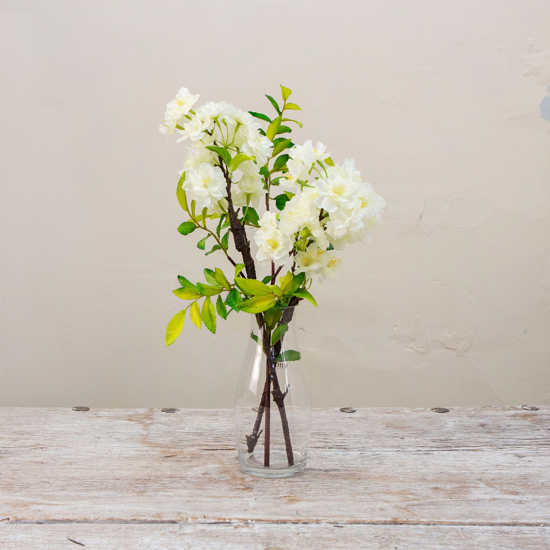 Artificial blossom stems arranged in a clear glass milk bottle vase