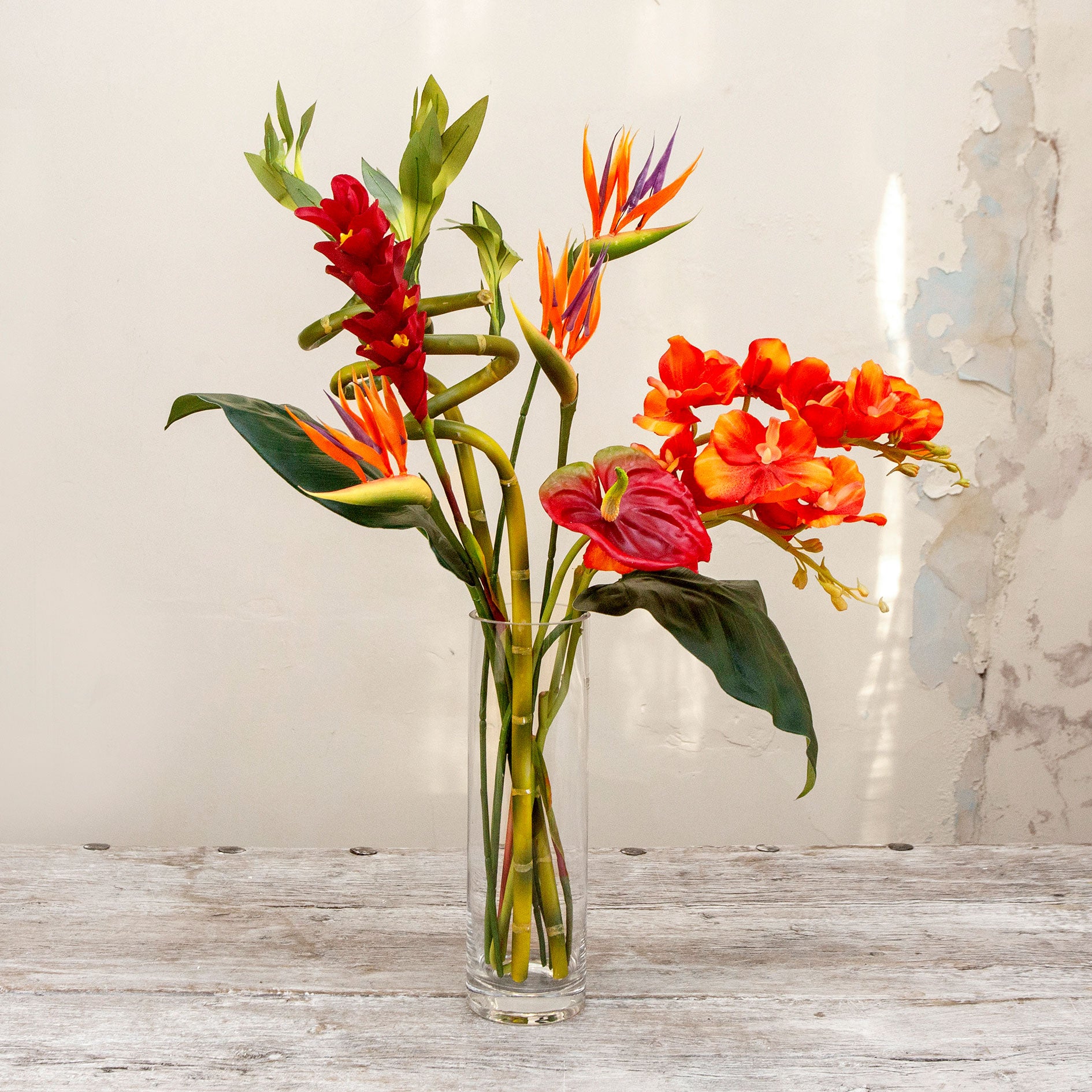 Artificial t ropical flower arrangement with orchids and birds of paradise in a glass cylinder vase