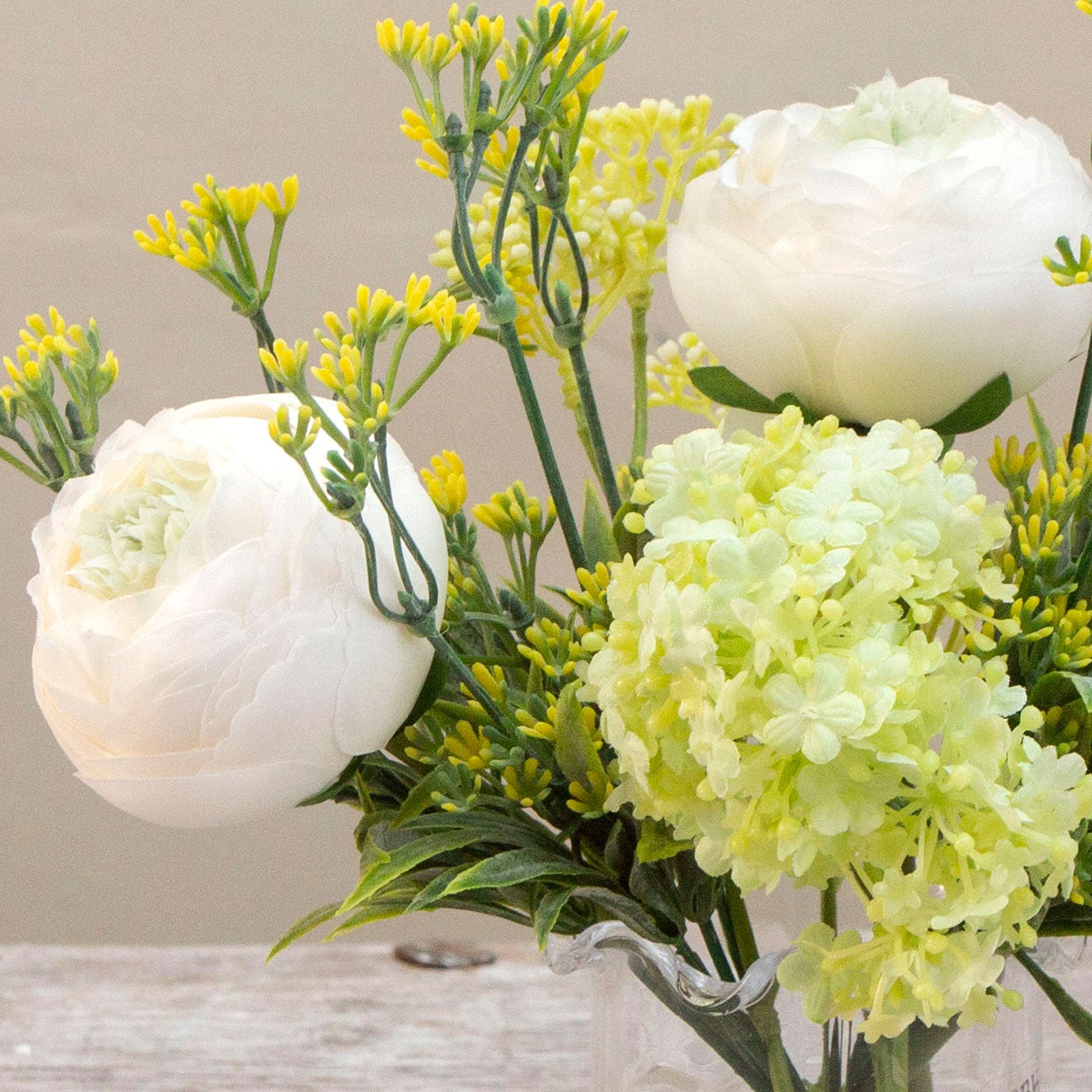 Artificial ranunculus and foliage arrangement in a clear glass garlic vase