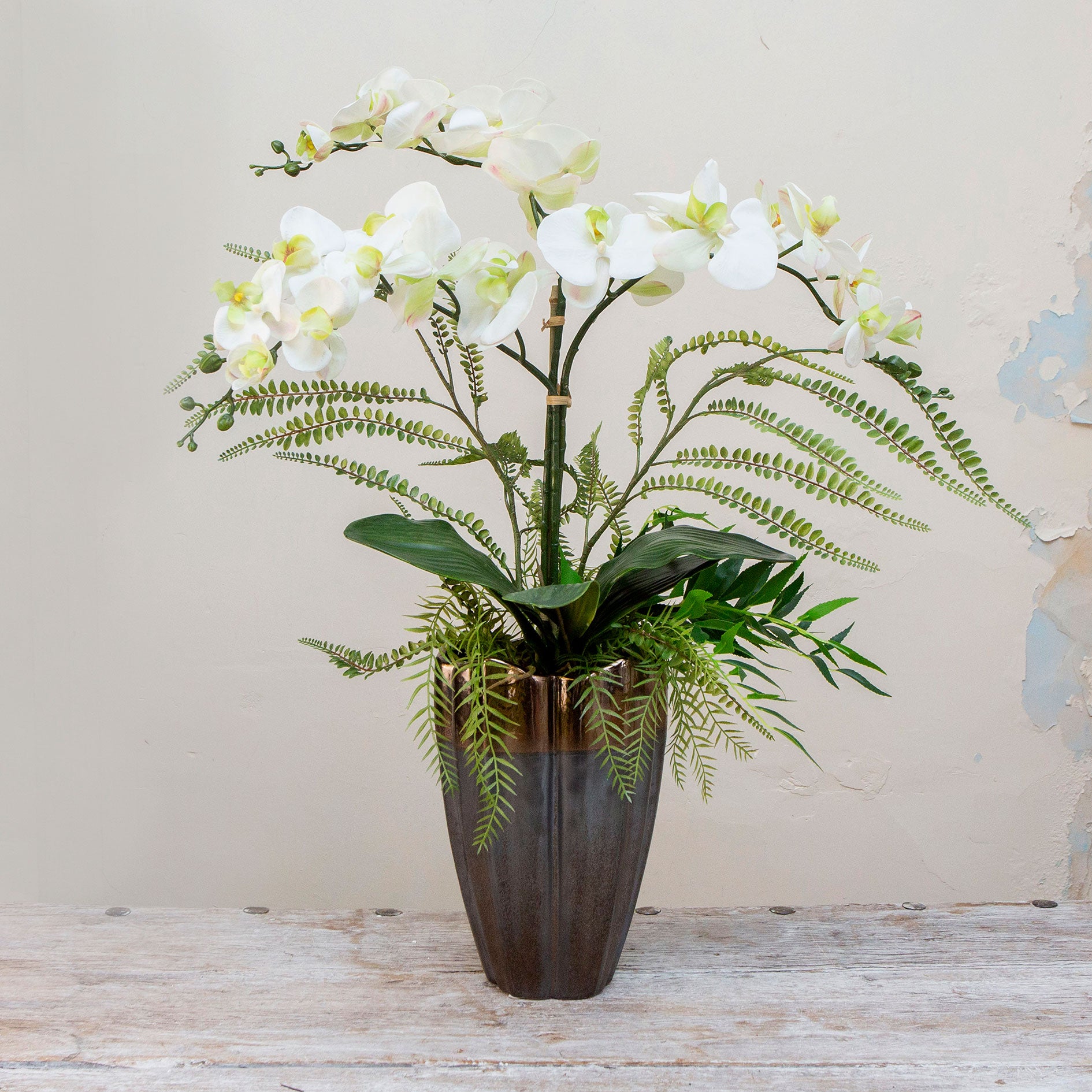 Artificial phalaenopsis orchid and ferns arranged in a tall lotus style pot