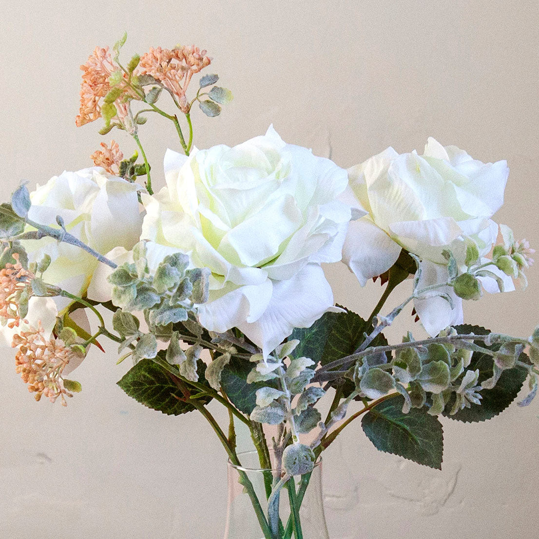 Close-up of artificial white roses and patrinia set in a clear glass milk bottle vase