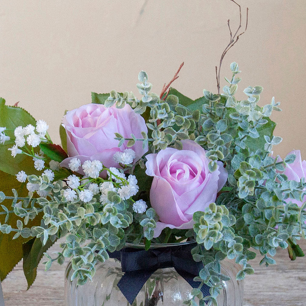 Close-up of artificial pink roses, mini eucalyptus and gypsophila set in a clear optic glass jar vase.