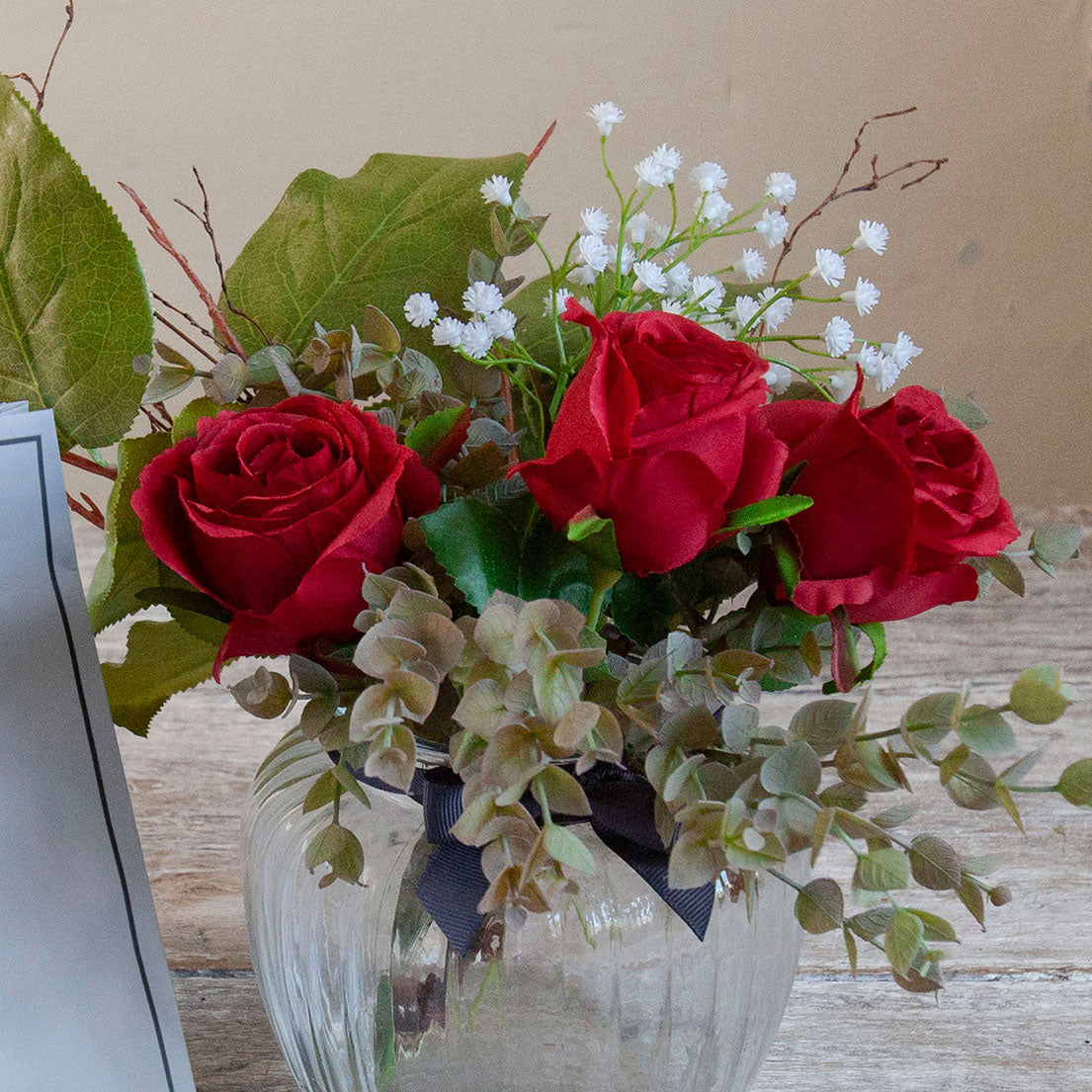 Close-up of artificial red roses, mini eucalyptus and gypsophila set in a clear optic glass jar vase.