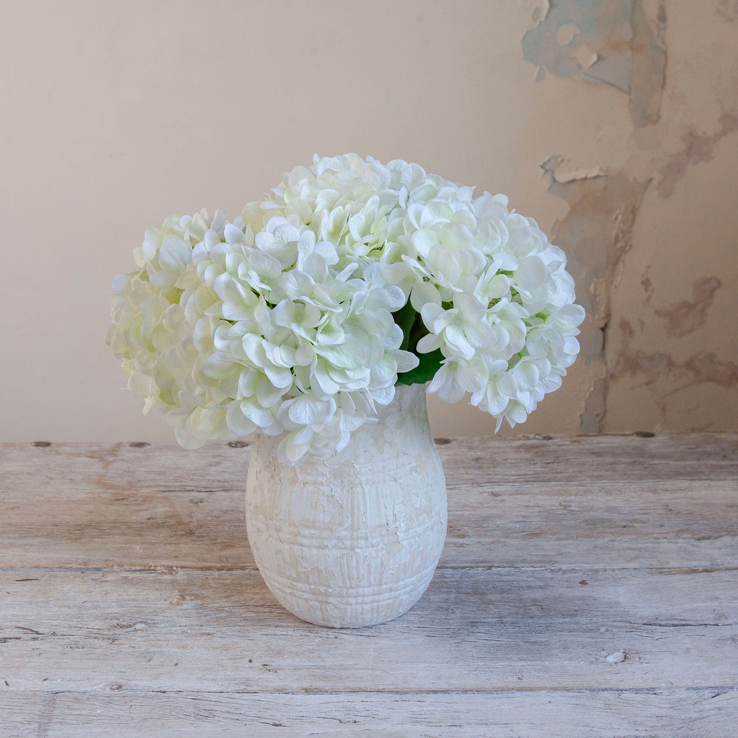 Artificial white hydrangea arrangement in a rustic textured white pot.