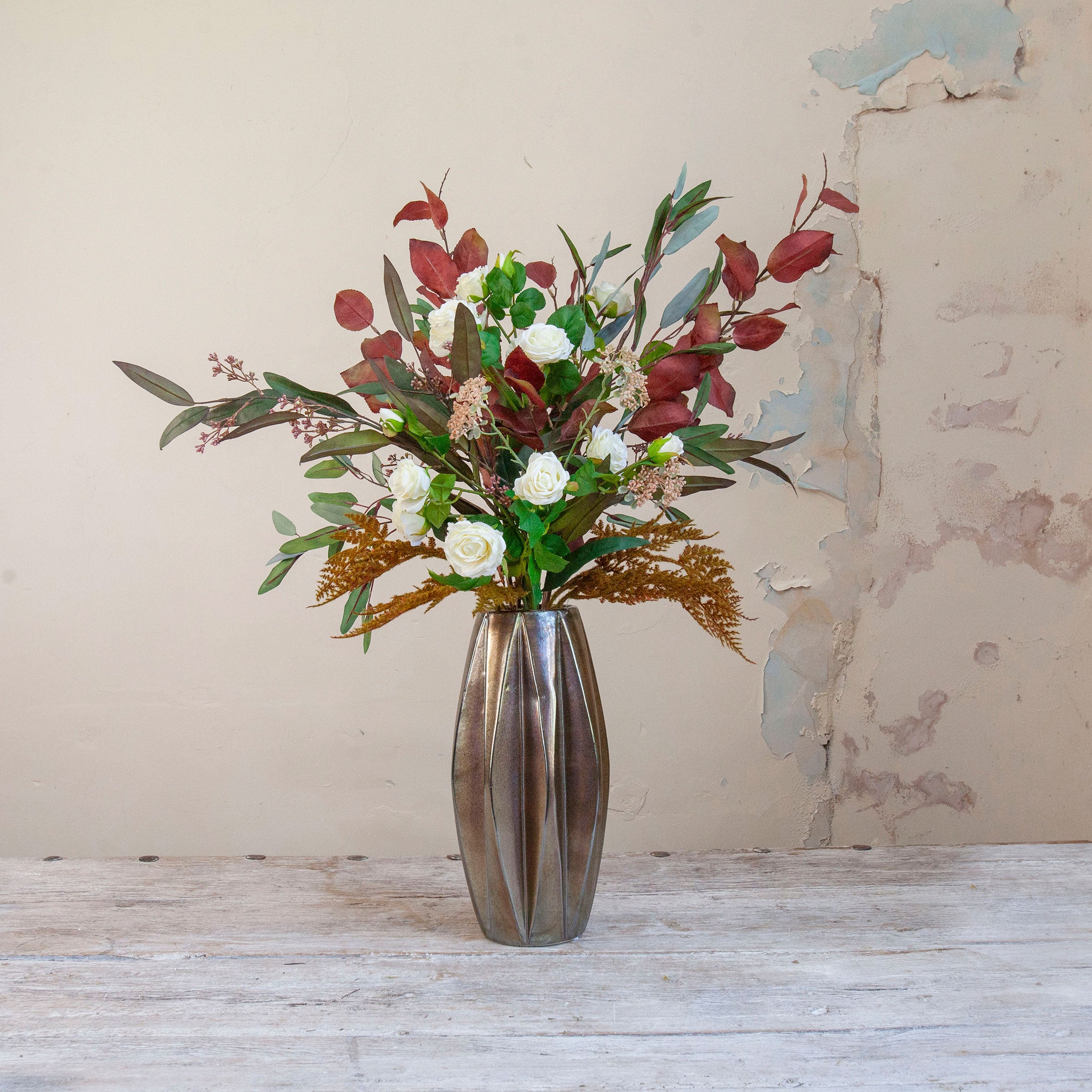 Artificial rose and berry arrangement with autumn foliage in a tall bronze geometric pot.
