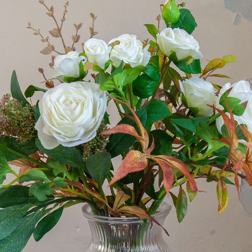 Close-up of artificial white roses and ranunculus with realistic green and warm autumn foliage.