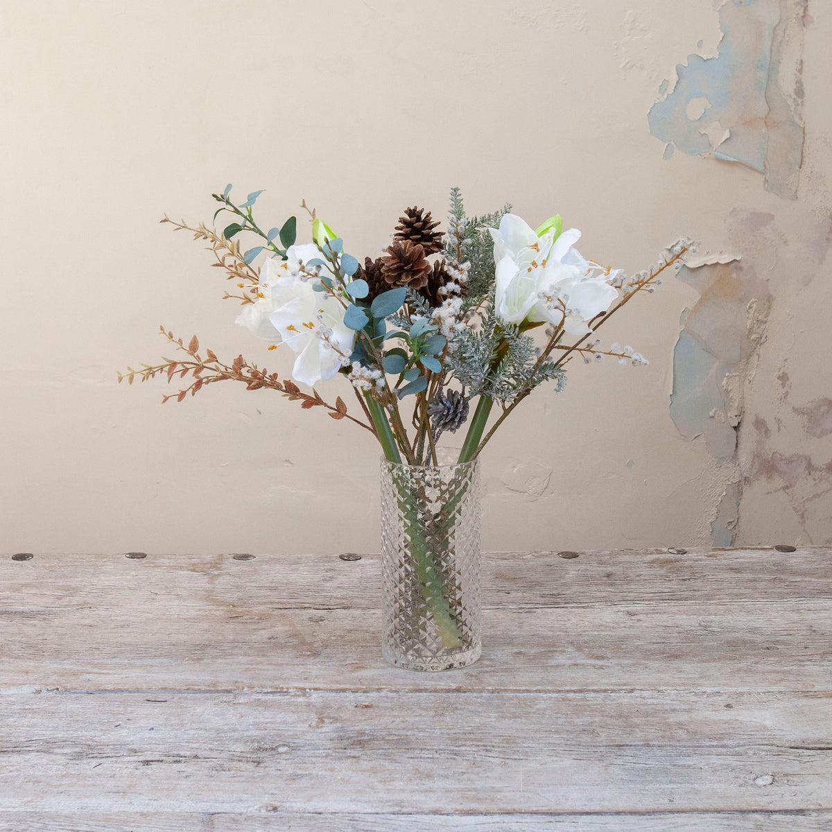 Artificial Amaryllis, Pine Cone & Eucalyptus Arrangement with white amaryllis blooms, brown pine cones, frosted winter foliage and eucalyptus in a textured clear cylinder glass vase