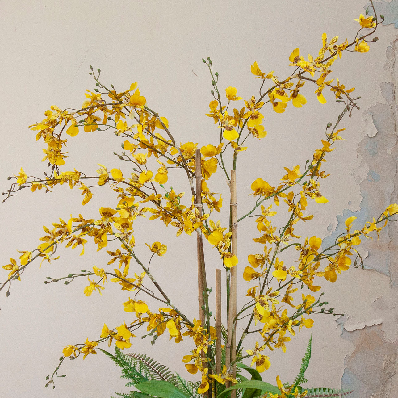 Close-up of artificial yellow dancing orchids with realistic branching stems and fern foliage.