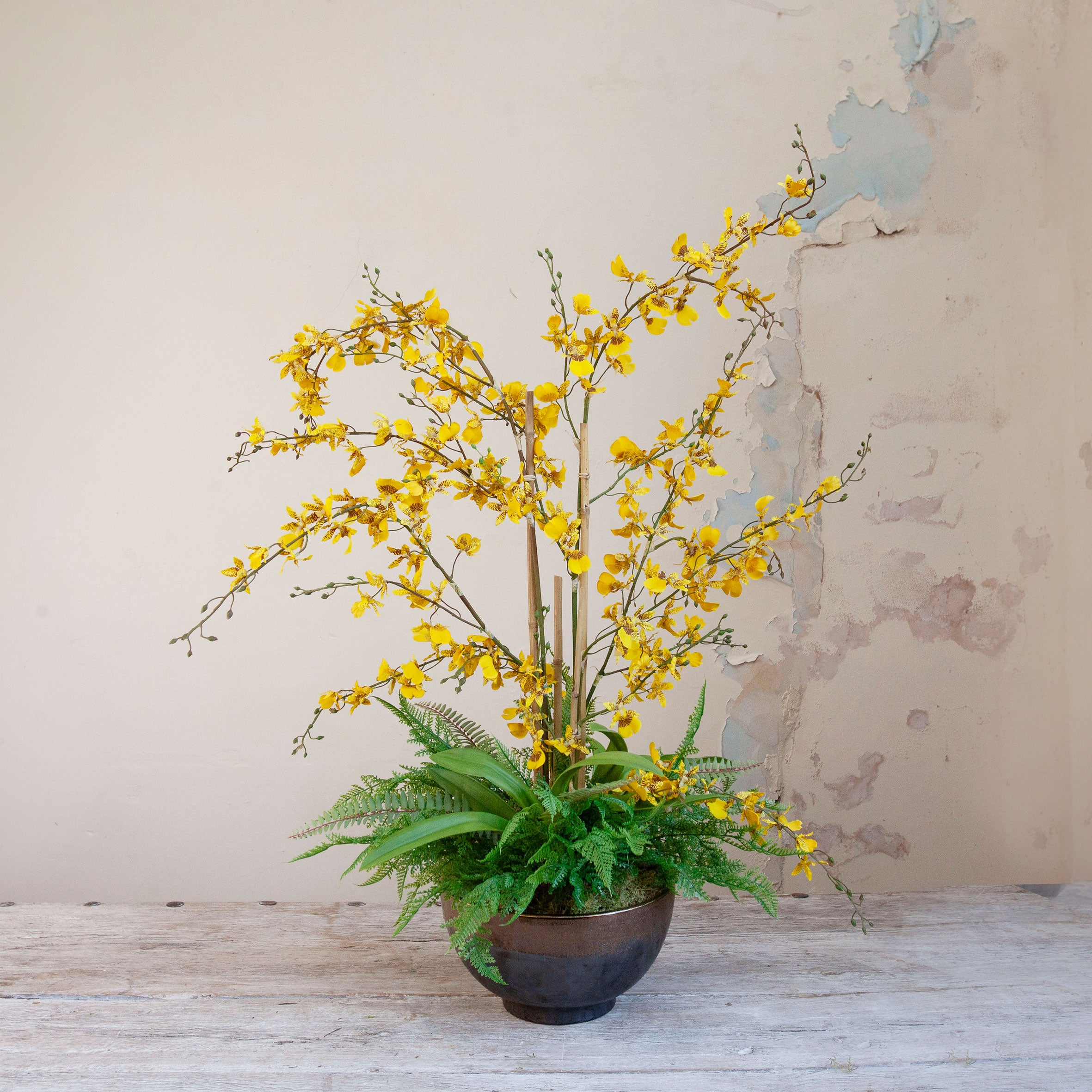 Artificial yellow Dancing Orchids with fern foliage arranged in a bronze footed bowl