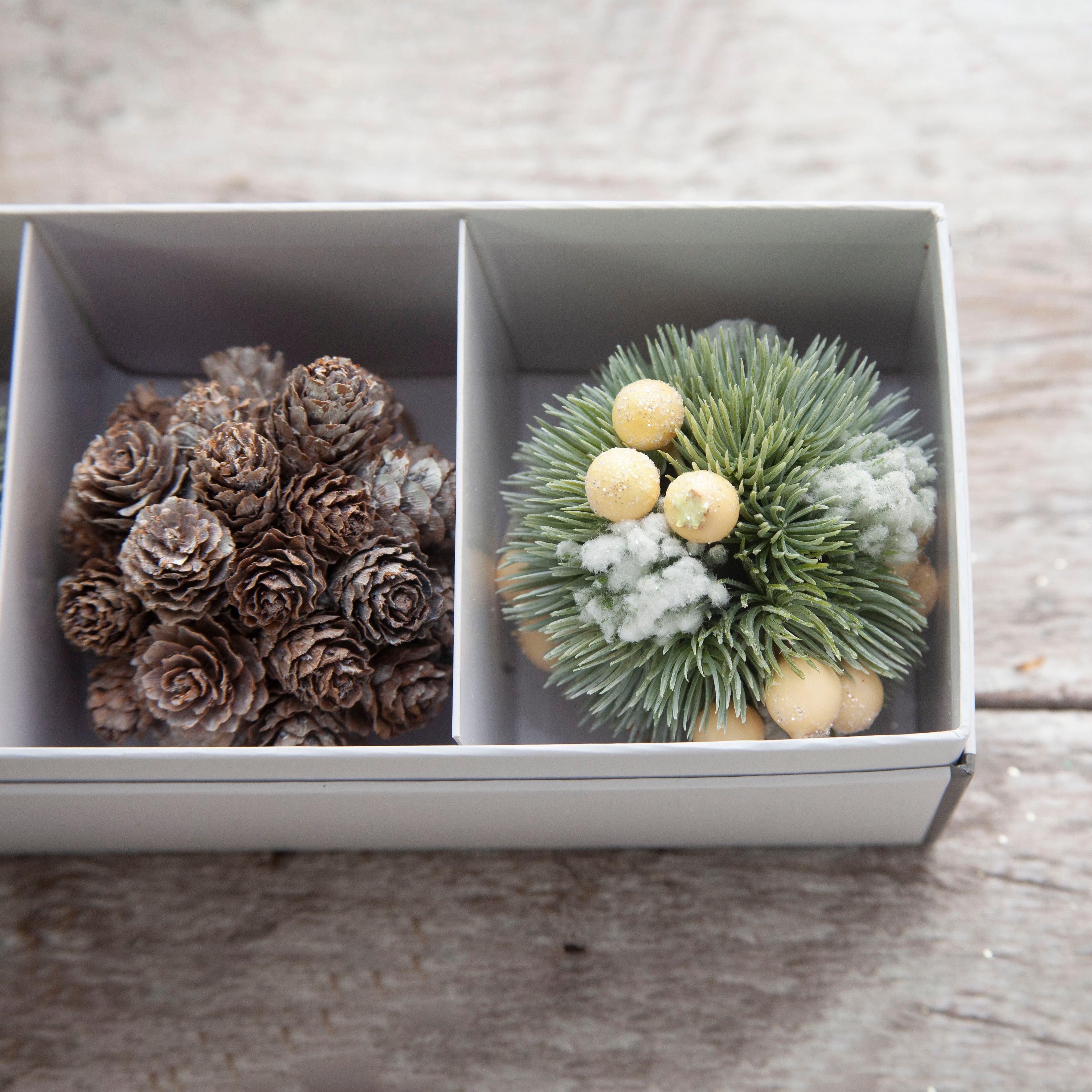 Close up view of the set of three artificial Nordic hanging balls with berries and pine cones on a wooden surface.
