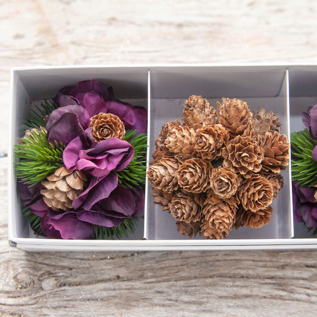 Close up view of the set of three decorative artificial f hanging balls with pine cones and hydrangeas displayed against a wooden background.