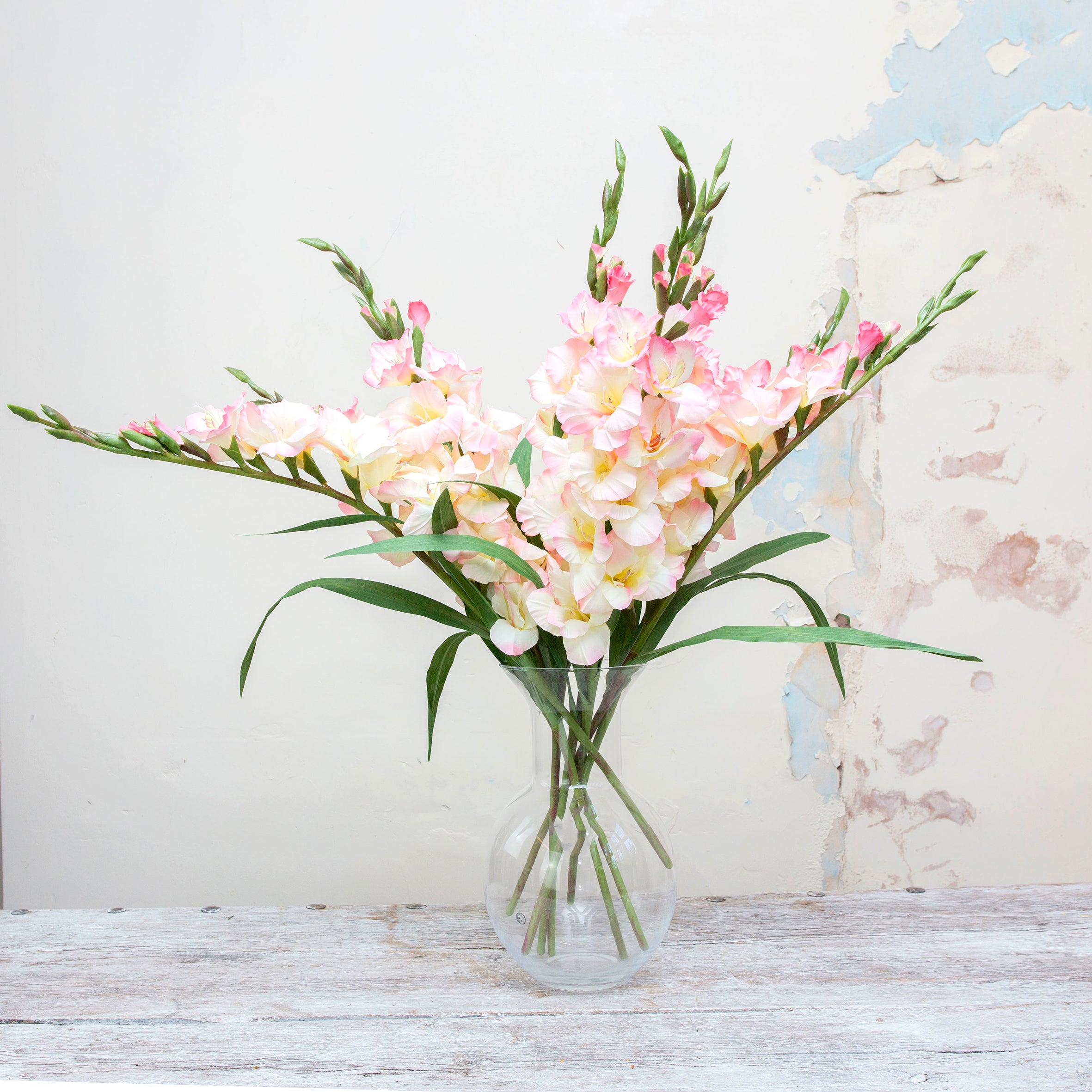 Artificial pale pink gladioli displayed in a in a clear vase, for styling purposes