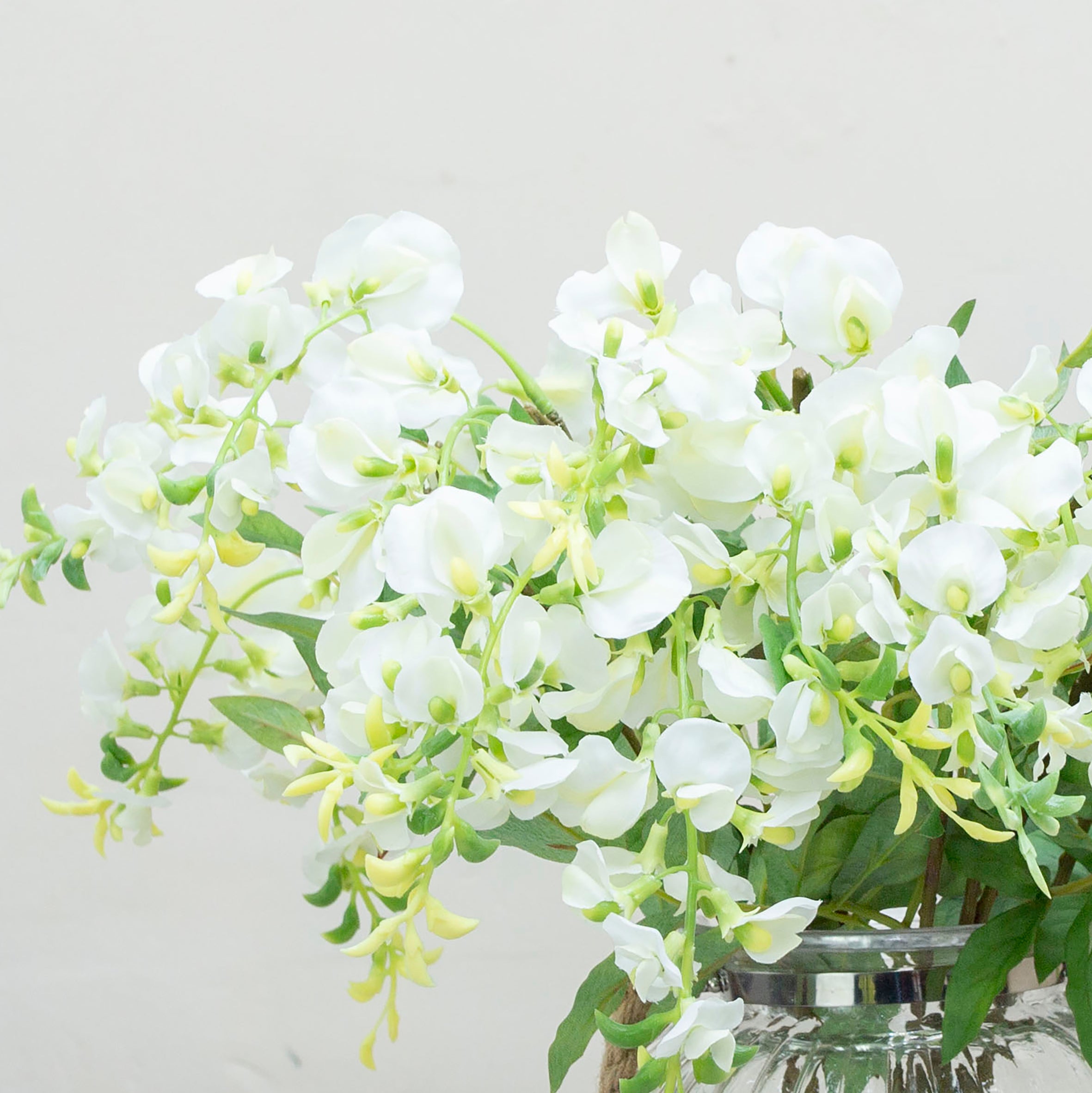 Close-up of artificial white wisteria flowers, showing softly layered petals, pale green bud detail and natural colour variation