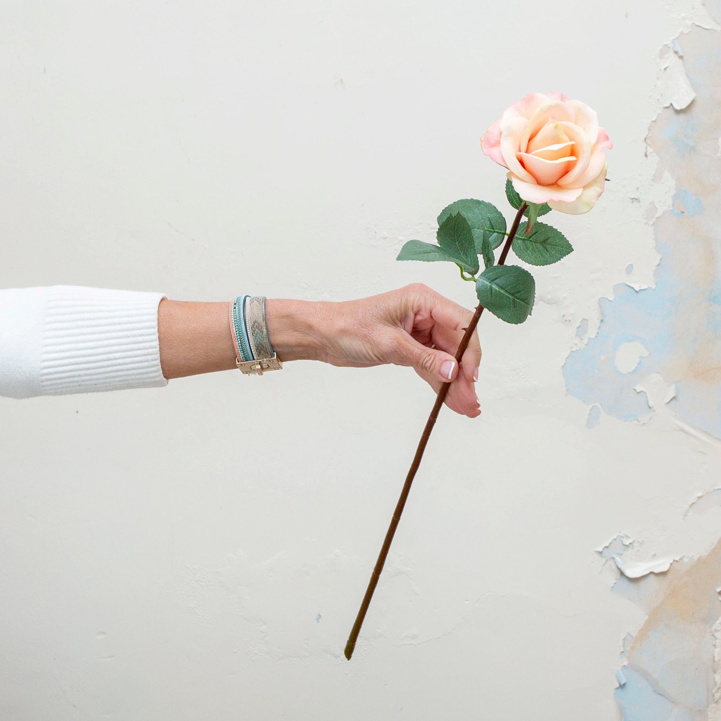 Artificial rose stem being held in hand, featuring a soft peach rose bloom with blush-pink tones and realistic green foliage on a long slender stem