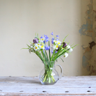 Artificial spring flower arrangement with daffodils, bluebells, and fritillaria arranged in a clear glass jug.