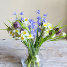 Artificial spring flower arrangement with daffodils, bluebells, and fritillaria arranged in a clear glass jug.
