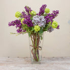 Artificial lilac and viburnum arrangement  in a clear glass vase