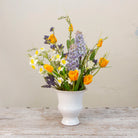 Artificial spring flower arrangement with daffodils and tulips in a white ceramic glazed urn