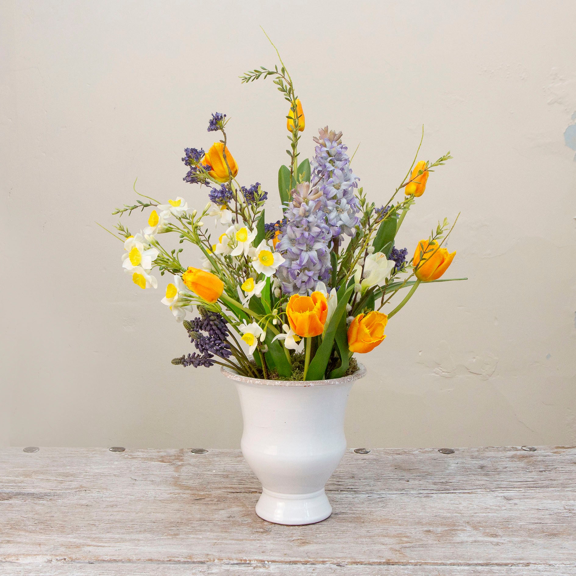Artificial spring flower arrangement with daffodils and tulips in a white ceramic glazed urn