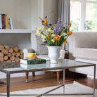 Artificial spring flower arrangement with daffodils and tulips in a white ceramic glazed urn