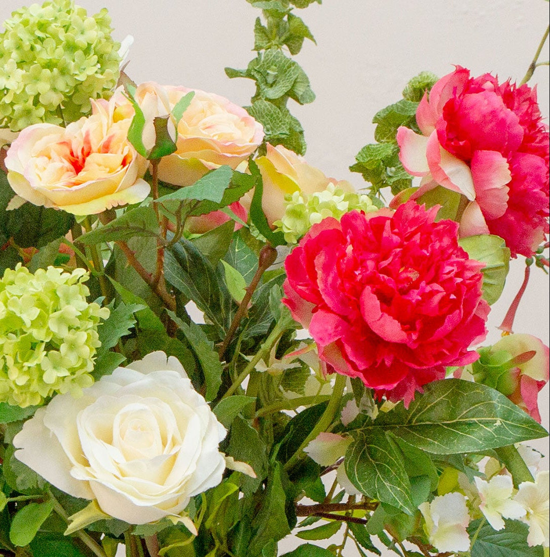 Artificial peach and lemon floral arrangement in a clear glass vase with roses, peonies, honeysuckle and viburnum