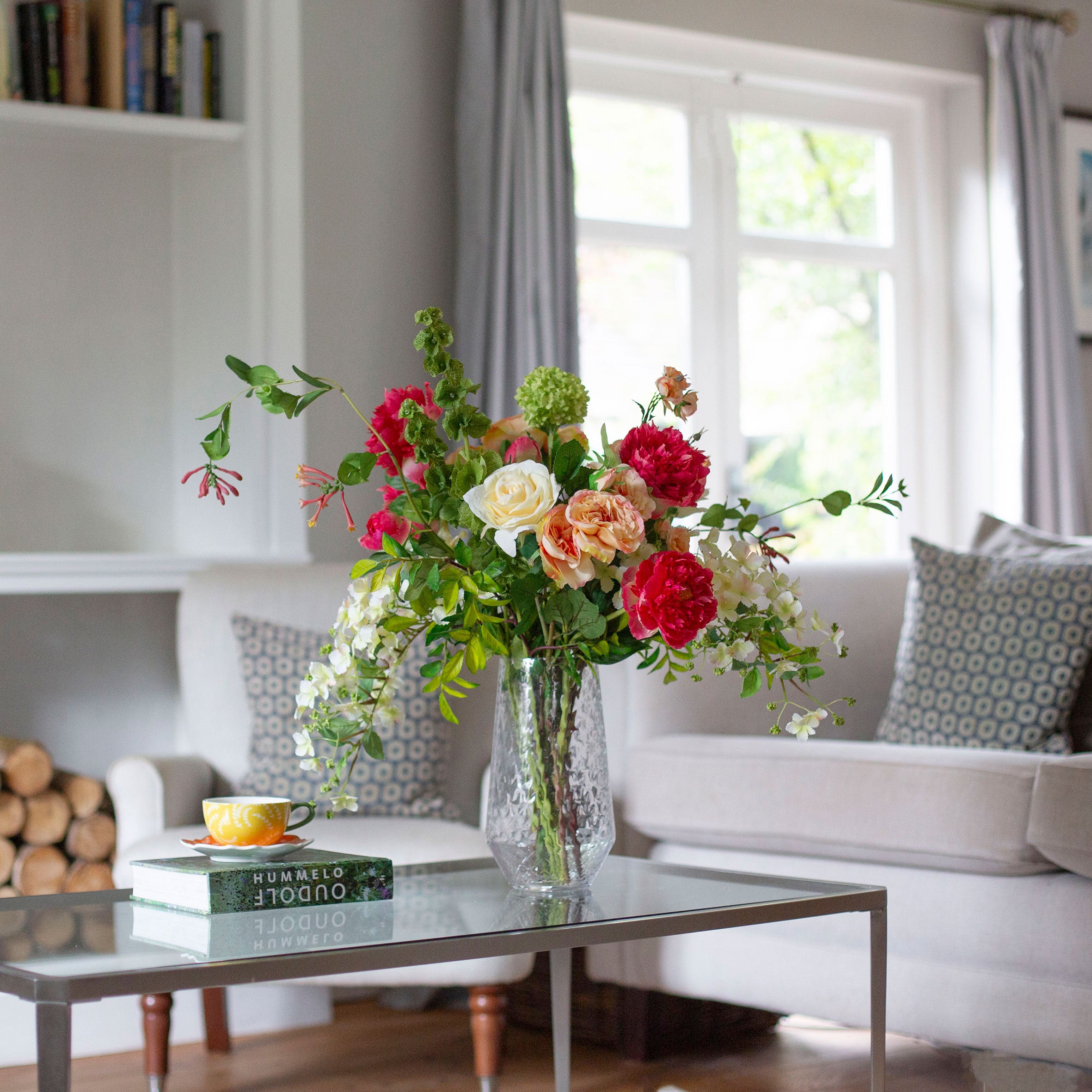 Artificial peach and lemon floral arrangement in a clear glass vase with roses, peonies, honeysuckle and viburnum