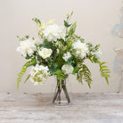 Artificial white and greenery faux flower arrangement with hydrangea, dahlia, snowball blooms and ferns in a glass Hampton vase