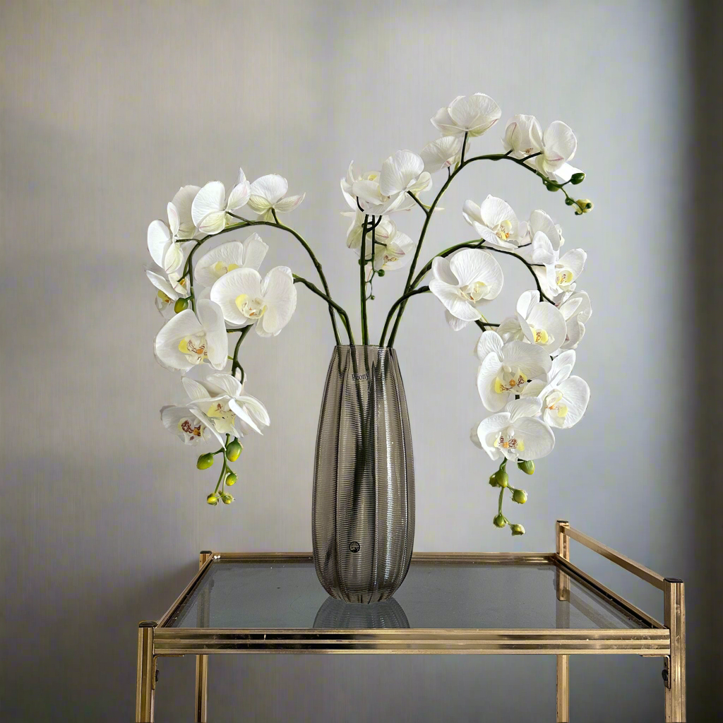 Artificial white orchid stem displayed in a vase, with realistic open blooms and delicate bud detail.