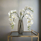 Artificial white orchid stem displayed in a vase, with realistic open blooms and delicate bud detail.