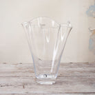 Handkerchief vase in clear glass with wavy flared rim on rustic wooden table.
