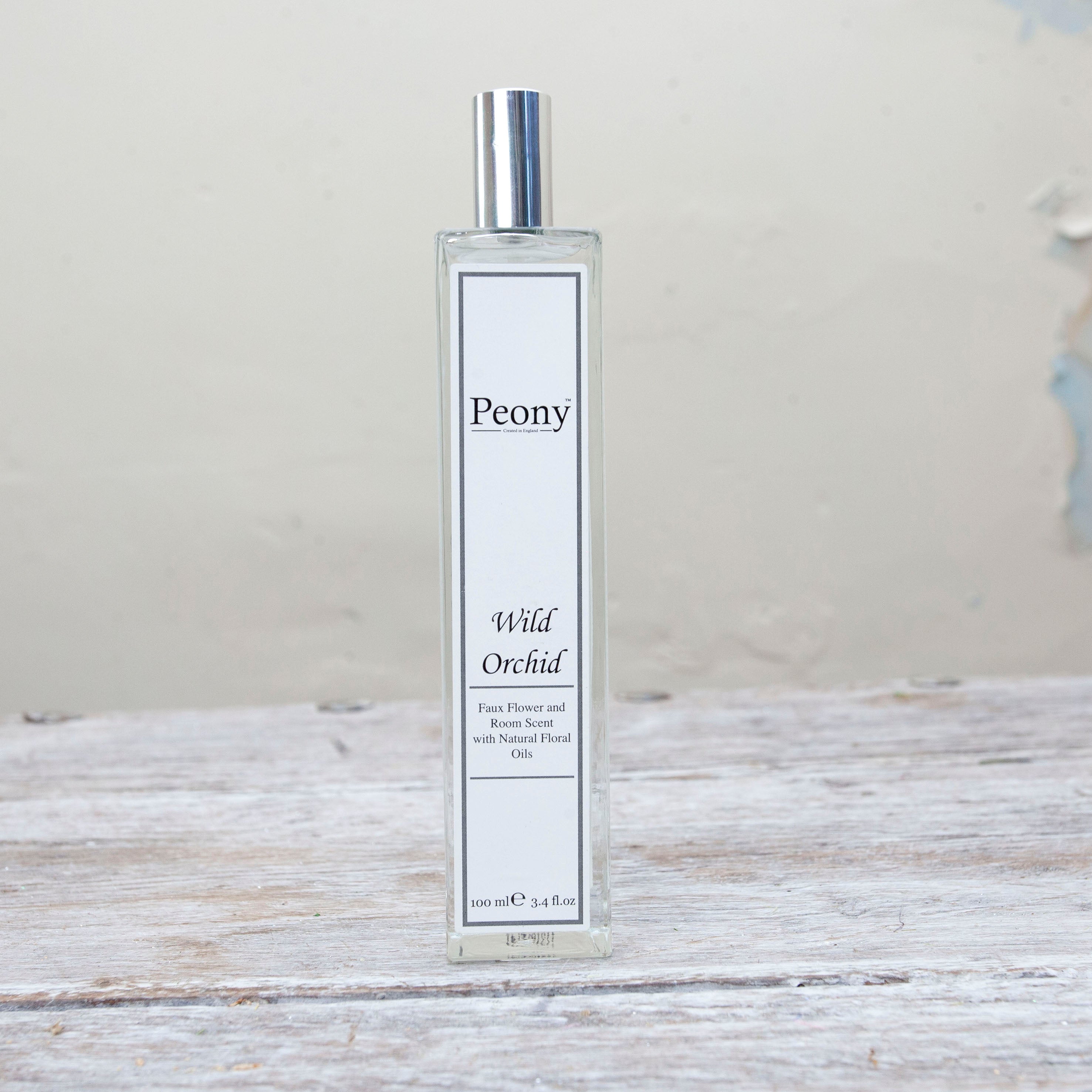 A bottle of 'Peony Wild Orchid' fragrance with a white label on a wooden surface.
