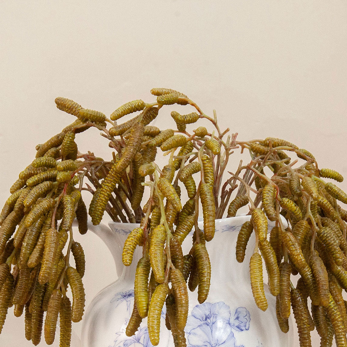 Close up of artificial green birch foliage spray stem displayed in a blue and white floral ceramic vase