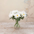 Artificial white chrysanthemum stems with green foliage displayed in a clear glass vase