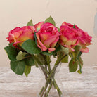 Close up of artificial pink rose stems with green foliage displayed in a clear glass vase